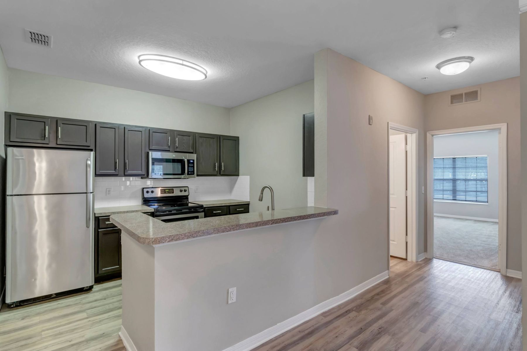 Empty room with wood floors, ceiling fan, and sliding glass door leading to a patio with vertical blinds at Apex West Midown.